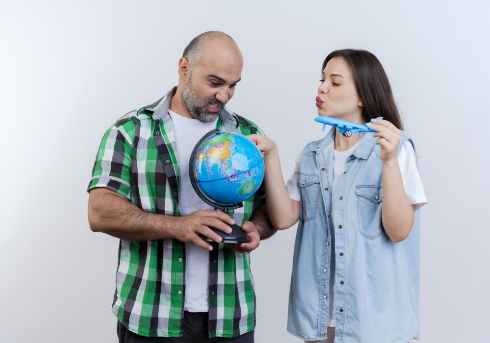 adult traveler couple impressed man holding globe and woman holding model plane touching globe and both looking at globe isolated on white background