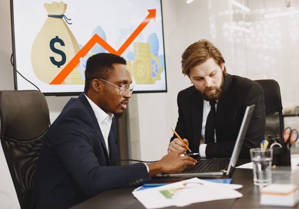 African man in a black suit. International partners. People sitting at the table with laptop.