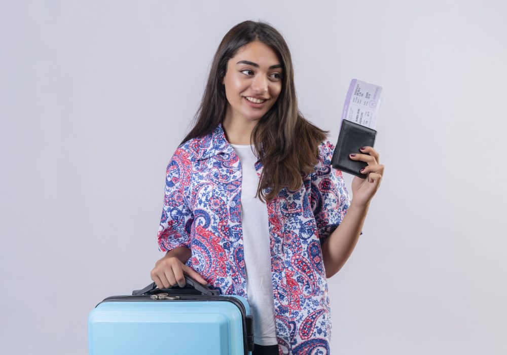 beautiful tourist woman holding travel suitcase and passport with tickets looking aside with smile on face happy and positive travel concept standing over white background