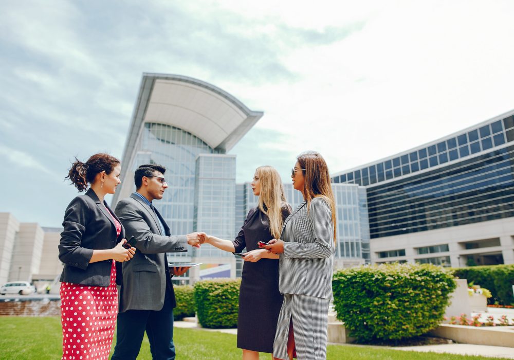 Handsome businessman in a city. Businessman in a glasses. Business partners in a summer city. Man and three women standingin a sity with tablet and phones