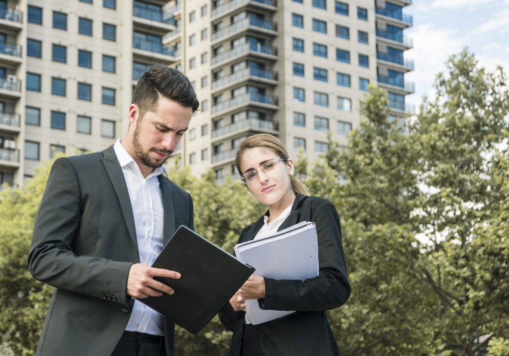 close-up-businessman-businesswoman-holding-documents-standing-front-building