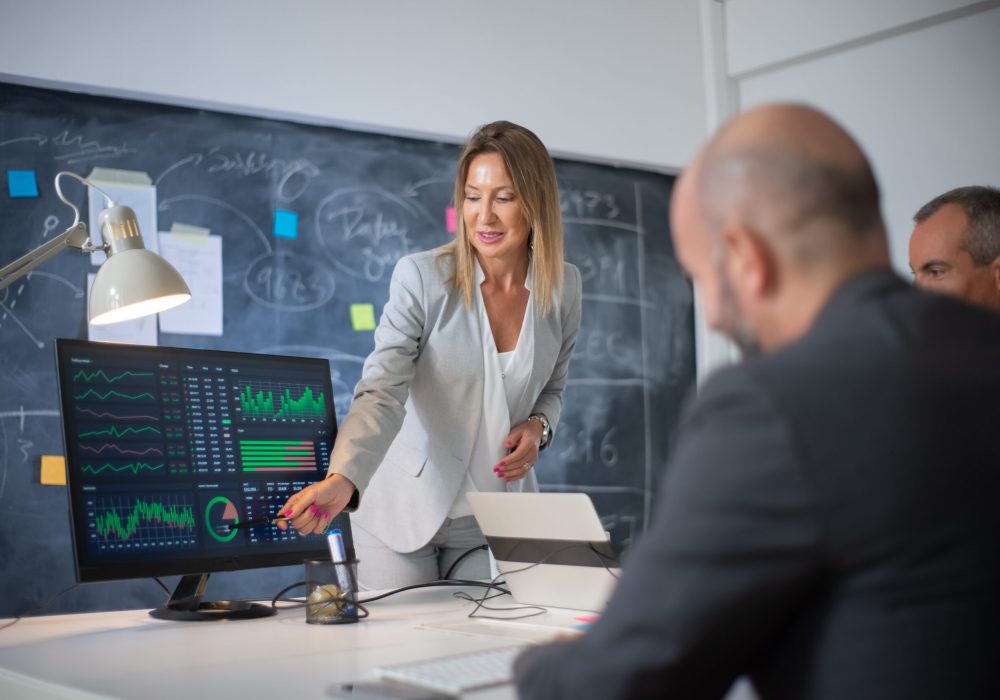 Company employees discussing market data on charts. Skilled woman leader and two men looking at diagrams on computer screen analyzing profit growth. Business growth and female business leaders concept