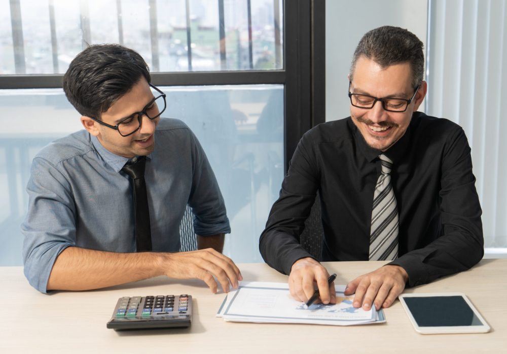 Jolly business partners discussing sales development at meeting. Happy excited businessmen examining papers and enjoying teamwork in office. Report concept