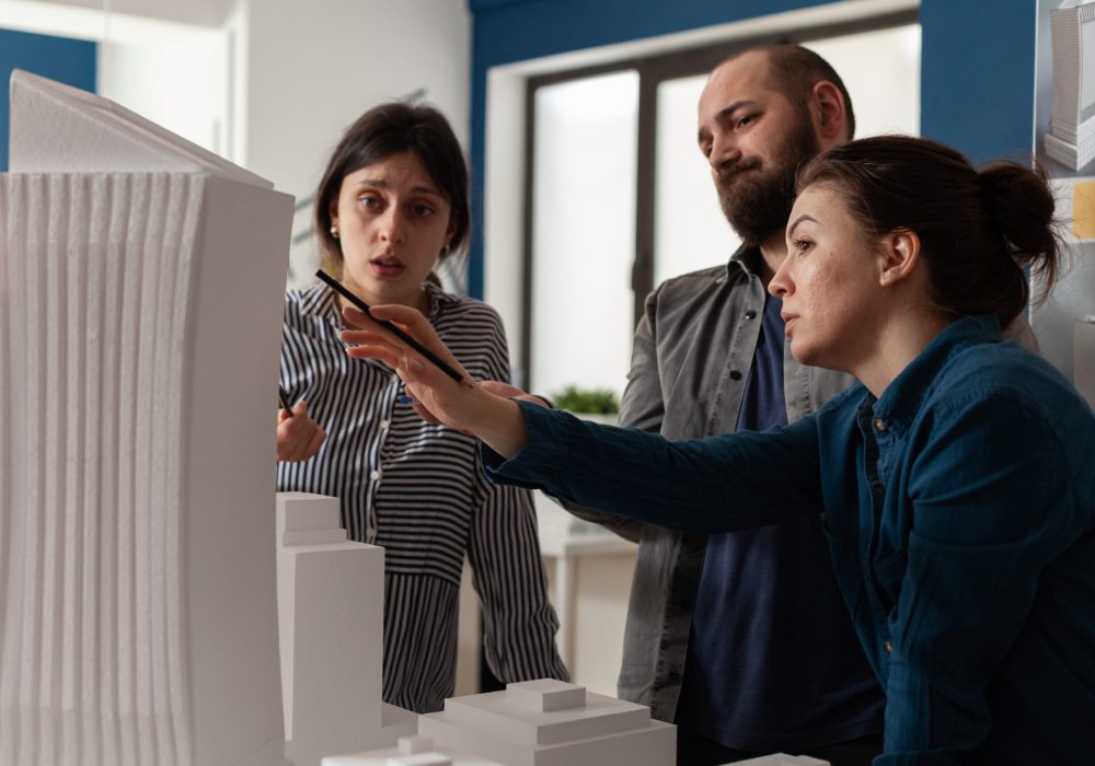 Professional team of architects analyzing maquette building model. Group of engineer partners working on project design for construction plan explaining modern blueprint vision.