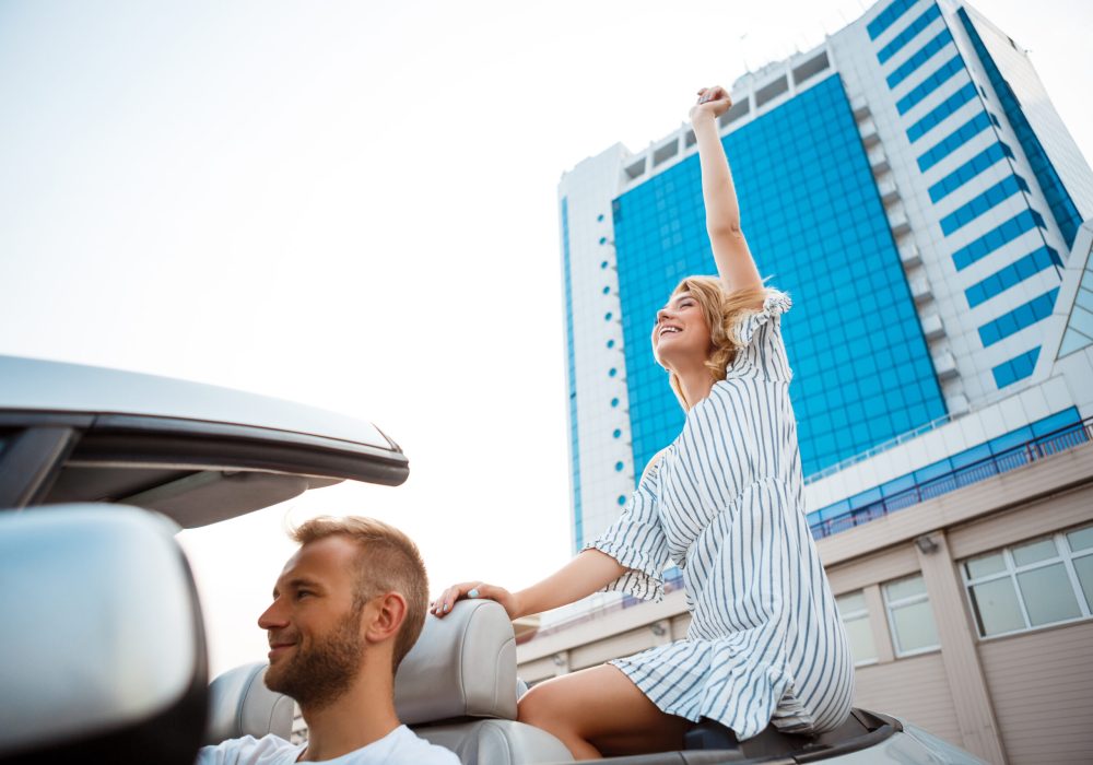 Young beautiful couple smiling, rejoicing, sitting in car near sea.